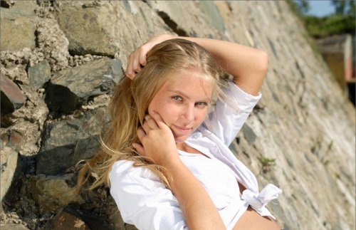 Милая блондинка с сексуальной попкой и бритой киской у каменной стены